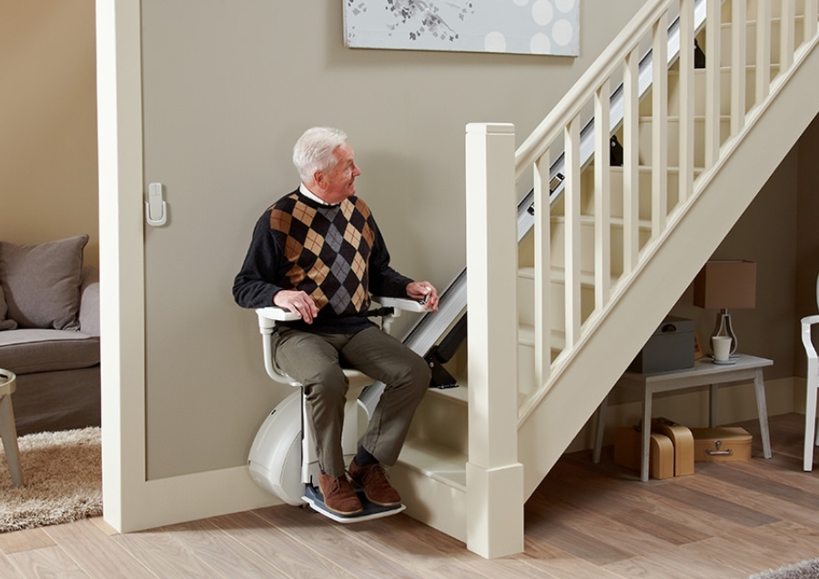 Ein älterer Mann nutzt einen Treppenlift in seinem Zuhause – ein Beispiel für barrierefreies Wohnen und praktische Lösungen in der Pflege zu Hause. Das Bild verdeutlicht, wie technische Hilfsmittel den Alltag erleichtern und die Selbstständigkeit fördern. Die IAHA (International Association for Healthy Aging) setzt sich für altersgerechte Wohnkonzepte ein, um sicheres und gesundes Altern im eigenen Zuhause zu ermöglichen.